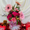 Pink roses and gerbera daisies in a heart-patterned gift box with a teddy bear