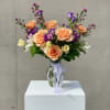 Peach and purple bouquet in a clear glass vase with a ribbon