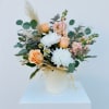 Peach and white floral arrangement in a white vase with eucalyptus