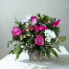 Pink roses and white daisies in a glass vase with a striped ribbon