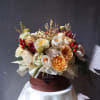 Mixed bouquet of cream, peach, and burgundy flowers in a round box