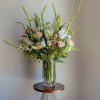 Tall bouquet of pale roses, white lilies, and greenery in a clear glass vase