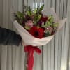 Handheld bouquet of red gerbera daisies, pink carnations, and lily buds wrapped in pale pink paper