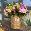 Pink and green floral arrangement in a gold hatbox