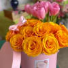 Pink tulips and orange roses in a pink hatbox with ribbon