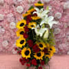 Bouquet of red roses, sunflowers, and white lilies against a pink rose wall
