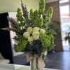 Tall green and white floral arrangement in a glass vase with a burlap bow