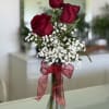 Three red roses in a glass vase with white baby's breath and a red ribbon