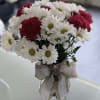 Bouquet of white daisies and red carnations in a glass vase with a lace ribbon