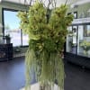 Tall arrangement of green orchids with trailing greenery in a glass vase