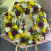 Circular floral wreath with red roses, white chrysanthemums, and yellow blooms on an easel