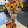 Bouquets of sunflowers and pink carnations wrapped in brown paper in a glass vase