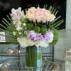 Large pastel floral arrangement in a glass vase with roses, orchids, and hydrangeas