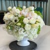 White floral arrangement in a white pedestal vase with green accents