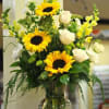 Tall arrangement of yellow sunflowers and white roses in a clear glass vase