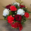Red roses and white and red carnations in a red gift container with gold accents