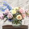 Pastel roses and blue flowers arranged in a clear glass vase