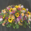 Casket spray with sunflowers, roses, and purple blooms on a dark drape