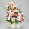 Pink and white mixed bouquet in a white ceramic vase with a teddy bear decoration.