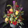 Mixed floral arrangement with yellow roses, red blooms, and a green artichoke in a gray vase