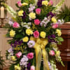 Standing floral spray with pink roses, yellow carnations, and purple blooms tied with a yellow ribbon