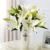White lilies arranged in a tall white vase with a cross emblem