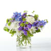 Blue, purple, and white flowers arranged in a clear glass vase