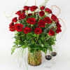 Red roses arranged in a glass vase with greenery and two wine glasses