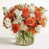 Orange roses and white flowers arranged in a clear glass vase