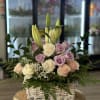 Basket arrangement of roses and lilies in soft pink, cream, and lavender