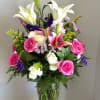 Tall white lilies arching above a rounded cluster of bright pink roses