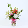 Mixed bouquet of lilies, chrysanthemums, and alstroemeria in a glass vase with a pink ribbon