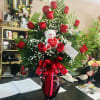 Red roses arranged in a vase with a teddy bear and heart decoration
