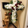 Large cross-shaped floral tribute with white lilies and red roses on a stand