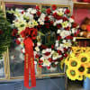 Heart-shaped floral wreath of red and white flowers on a stand with a red ribbon