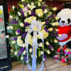 Large standing floral spray with white roses, lilies, and purple flowers on a ribboned easel