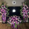 Three purple, pink, and white floral sprays with ribbon accents arranged around a TV.