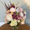 Pastel bouquet of roses, peonies, hydrangea, and purple accent flowers in a glass vase