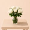 White roses arranged in a clear glass vase with greenery