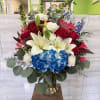 Bouquet of red roses, white lilies, and blue hydrangeas in a glass vase