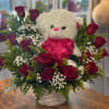 White teddy bear surrounded by red roses in a basket