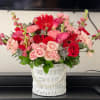 Pink and red mixed flower arrangement in a white basket vase