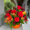 Red roses and mixed flowers arranged in an orange pumpkin vase