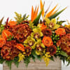 Orange roses and orchids arranged with tropical blooms in a wooden container