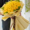 Bouquet of yellow roses wrapped in cream paper with a brown ribbon
