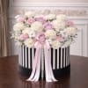 Round hat box of white carnations with pink and lavender roses, trimmed with pink ribbons and pearls