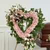 Heart-shaped pink floral funeral wreath on a stand beside a casket