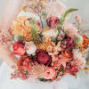 Handheld bouquet of orange, pink, and burgundy flowers