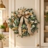 Round wreath with white flowers, greenery, and a burlap bow on a cabinet door