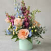 Pastel floral arrangement in a mint green box with peach roses and blue blooms